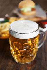 Glass mug of light beer with snacks on dark wooden table, close up