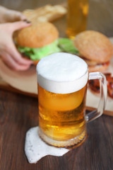 Glass mug of light beer with snacks on dark wooden table, close up