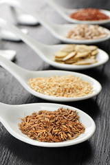 Different kinds of seeds in spoons on wooden table