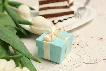 Sweet creamy cake with flowers and present box on wooden table closeup
