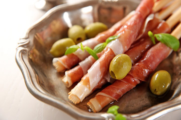 Bread sticks grissini with prosciutto ham, close up