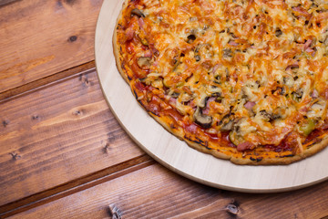 Flat lay Italian pizza with ham and mushrooms on a wooden round tray on wooden table top view