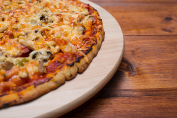 Italian pizza with ham and mushrooms on a wooden board on natural wooden table