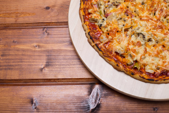 Flat lay Italian pizza with ham and mushrooms on a wooden round tray on wooden table top view