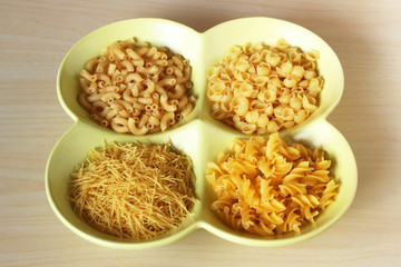 Dried pasta variety in shapes in bowl on table