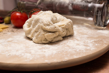 The preparation of pizza dough. On a wooden Board rolling pin is a bottle of wine and ingredients for pizza: tomatoes, cheese, basilic, olives.