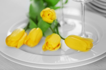 Set of dishes with yellow tulips for dinner party, close up