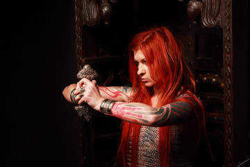 Studio shot of beautiful young redhead girl with multiple tattoo in chainded armour with the sword