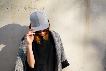 Female model wearing a black blank cap and sunglasses looking away. Portrait of a young beautiful girl with cap - 107591217