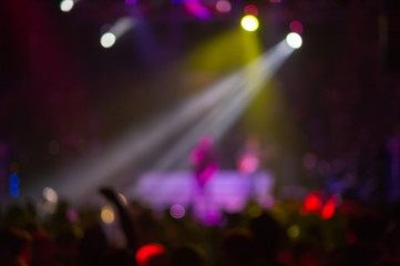 Blurred background : Club, disco DJ playing and mixing music for crowd of happy people. Nightlife, concert lights, flares
