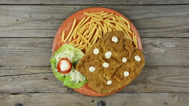 Large Wiener Schnitzel on a clay plate with fries,hand amounts steak on an old wooden table