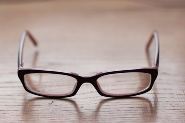 Close up of eyeglasses on the wooden office desk, blurred background