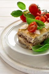 Homemade lasagna with bechamel sauce decorated basil leaves and cherry tomatoes on white plate