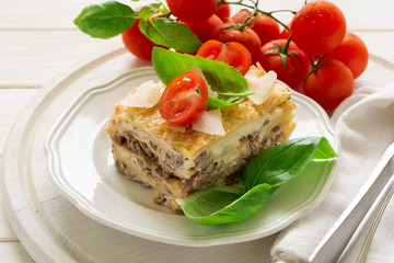 Homemade lasagna with bechamel sauce decorated basil leaves and cherry tomatoes on white plate