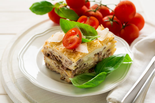 Homemade lasagna with bechamel sauce decorated basil leaves and cherry tomatoes on white plate