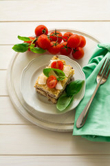 Homemade lasagna with bechamel sauce decorated basil leaves and cherry tomatoes on white plate
