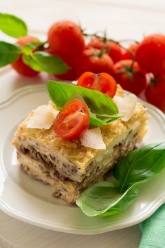 Homemade lasagna with bechamel sauce decorated basil leaves and cherry tomatoes on white plate