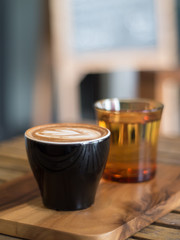Cup of Latte art coffee and and glass of water on wooden tray