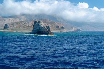 The rocky coast of the Mediterranean sea against the blue sky and clouds.