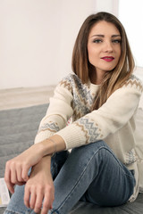 cute long-haired young woman in sweater and jeans sitting on the floor arms crossed looking seriously into camera vertical view