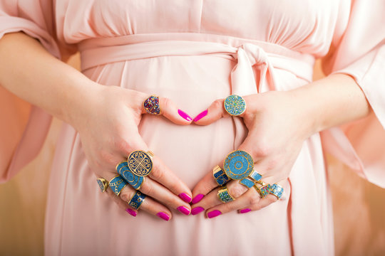 Pregnant woman with beautiful rings showing heart sign
