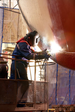 Shipyard Welder Welding The Hull Of The Ship At The Dock With Lift