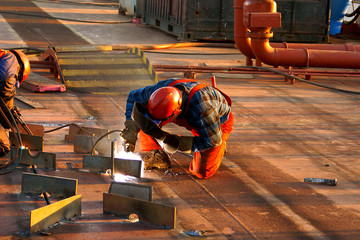 Shipyard welder during welding on the deck of the ship during the renovation - obrazy, fototapety, plakaty