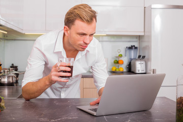 Man drinking coffee and using computer in kitchen