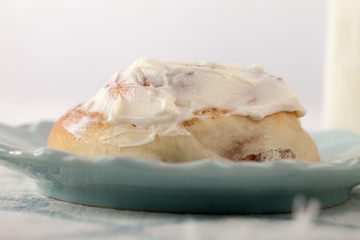 Freshly baked homemade cinnamon roll with cream cheese buttercream frosting and an antique bottle of milk macro shot
