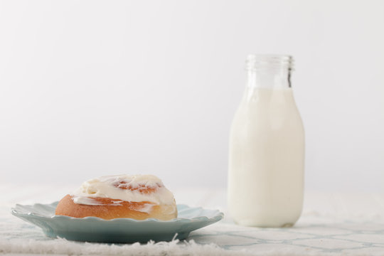 Freshly Baked Homemade Cinnamon Roll With Cream Cheese Buttercream Frosting And An Antique Bottle Of Milk With A White Background