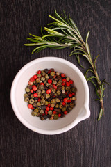 a mixture of peppers ( red, black , white ) in a white mortar with a sprig of rosemary