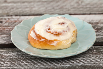 Freshly baked homemade cinnamon roll with cream cheese buttercream frosting on an old barn wood table