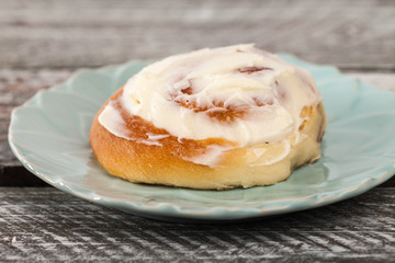 Close up of freshly baked homemade cinnamon roll with cream cheese buttercream frosting and an antique bottle of milk