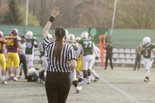 Female American football referee giving signals and blurred players in the background