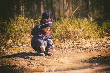 Little boy playing in puddle in spring