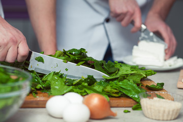 Vegetarian bakery concept. Chef's hands cutting feta cheese, spinach