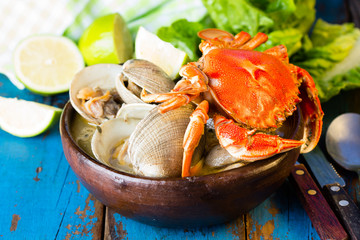 Seafood shellfish soup of clams and crabs in clay bowl on wooden blue background. Mariscal or paila marina