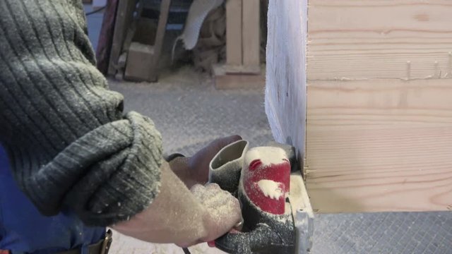 a man in a special uniform with his bare hands firmly holding an electric planer and performs the woodwork