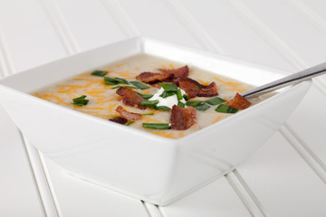 Homemade organic potato leek soup with Greek yogurt, Applewood smoked bacon, shredded cheddar cheese, and garlic chives close shot on white