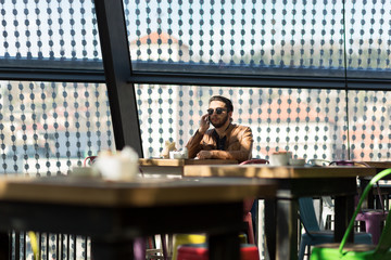 Happy hipster using smart phone at cafe sitting on chair