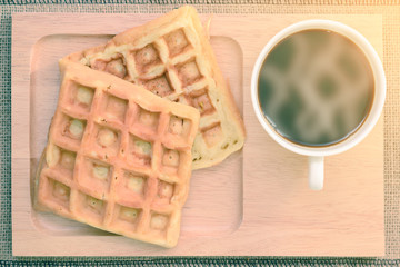 Top view of hot coffee and waffle on wooden coaster.