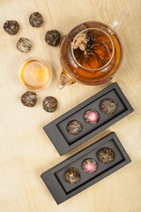 top view of exotic green tea glass teapot with floral blooming tea ball on wooden background