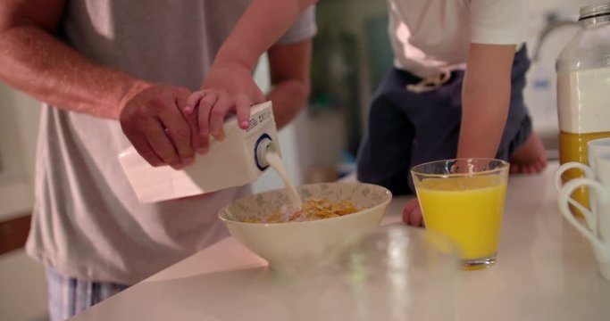 Father and son preparing cornflakes in a bowl with milk