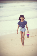 young girl walking by the sea with bucket in hand