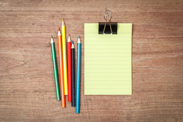 Green lined note paper with color pencils on wood table for back