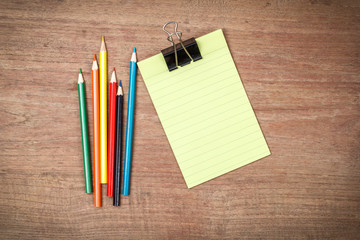 Obraz premium Green lined note paper with color pencils on wood table for back