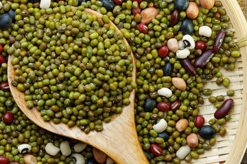 Mung beans in wooden spoon with mixed beans in rattan tray in the background