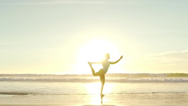 Happy young woman practicing yoga on the beach at sunset. Healthy active lifestyle concept. Slow Motion