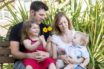 Young happy, smiling family, parents with two young children sitting in garden