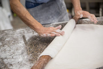 Hands baking dough with rolling pin on wooden table